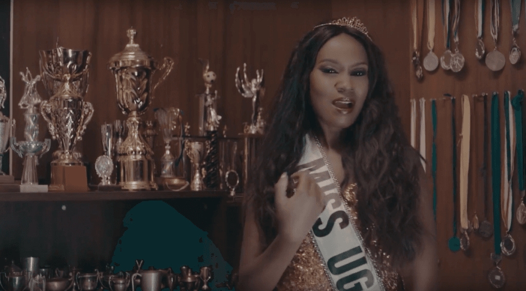 Juliana Standing infront of trophies with a Miss Uganda ribbon in Im Still Here Video - Spur Magazine